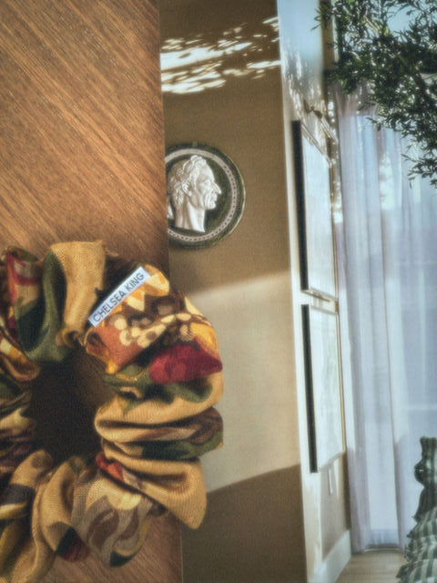 floral scrunchie with a visible brand label on a wall with a decorative plate.